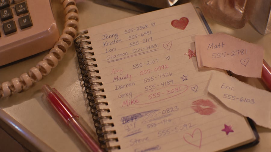 A spiral-bound notebook open to a page of handwritten names and phone numbers, with additional sticky notes for Matt and Eric placed on top.
