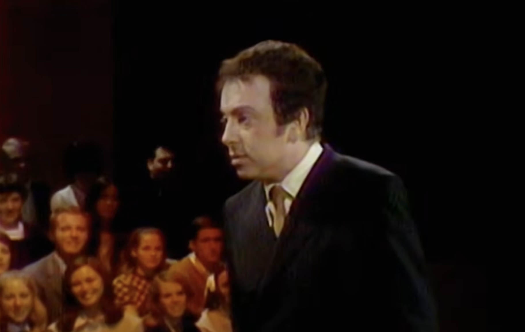 A man in a suit and tie standing in front of an audience.