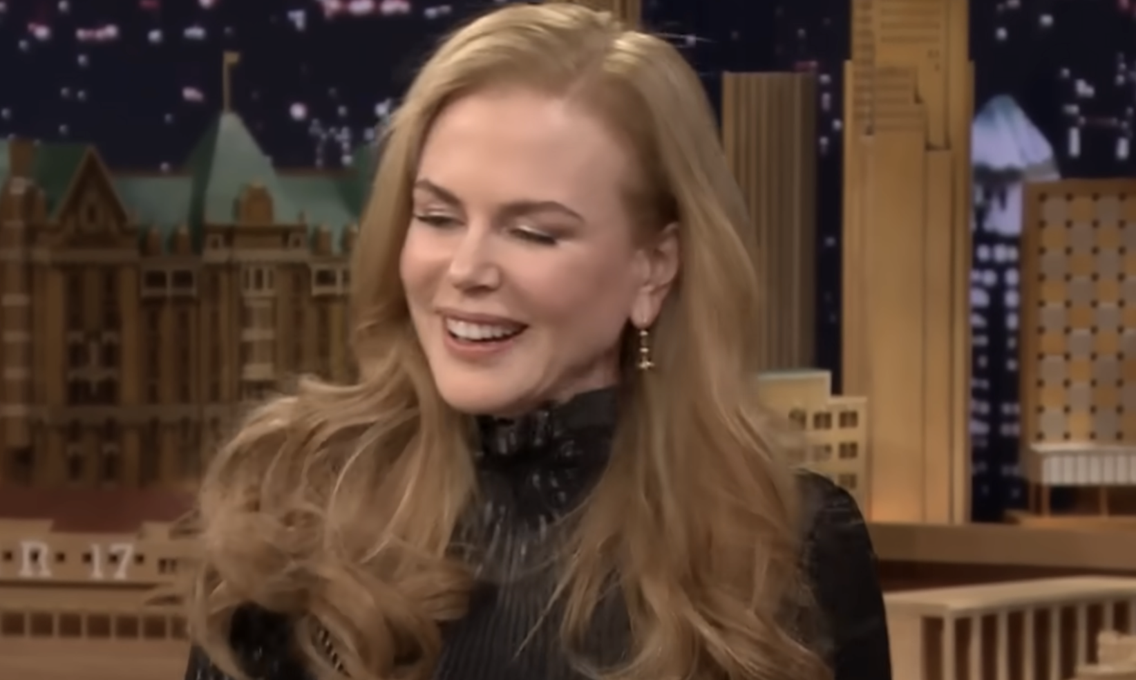 Nicole Kidman smiling during an interview on a talk show set.