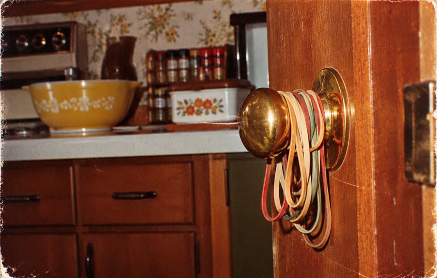 A collection of colorful rubber bands hanging from a brass door knob in a kitchen.
