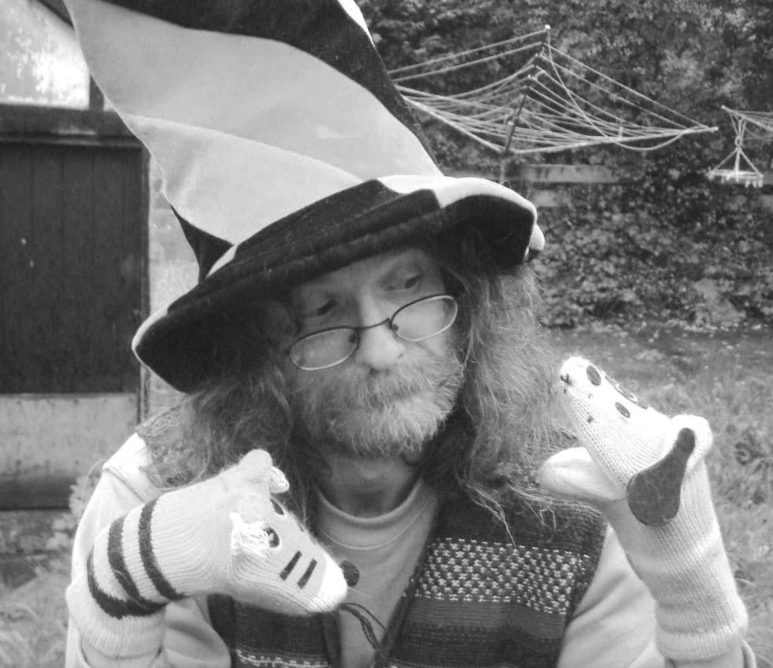 A person with long hair and a tall, striped hat performing with two sock puppets on their hands.
