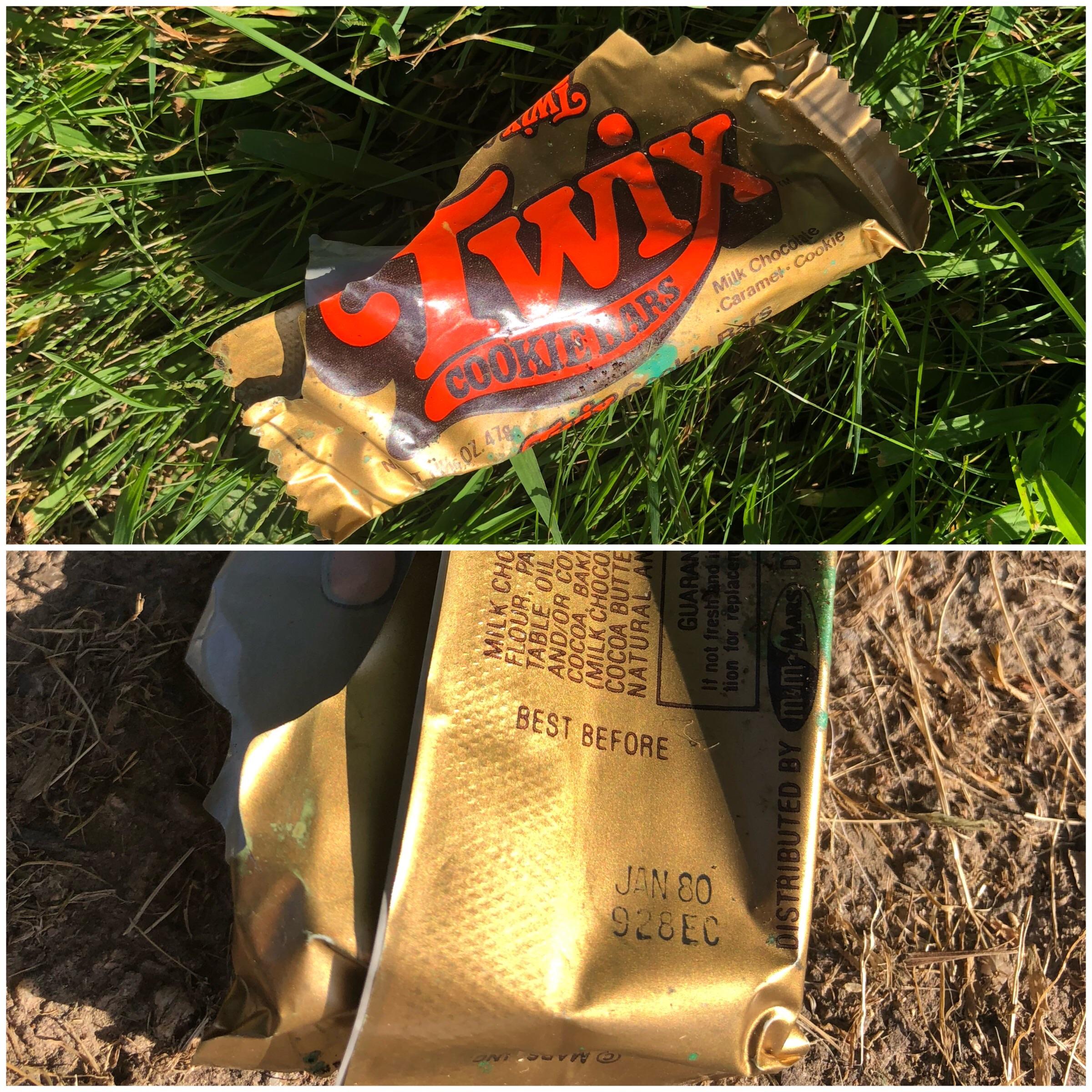 A discarded Twix candy bar wrapper in grass and on dirt, showing a best-before date of January 1980.