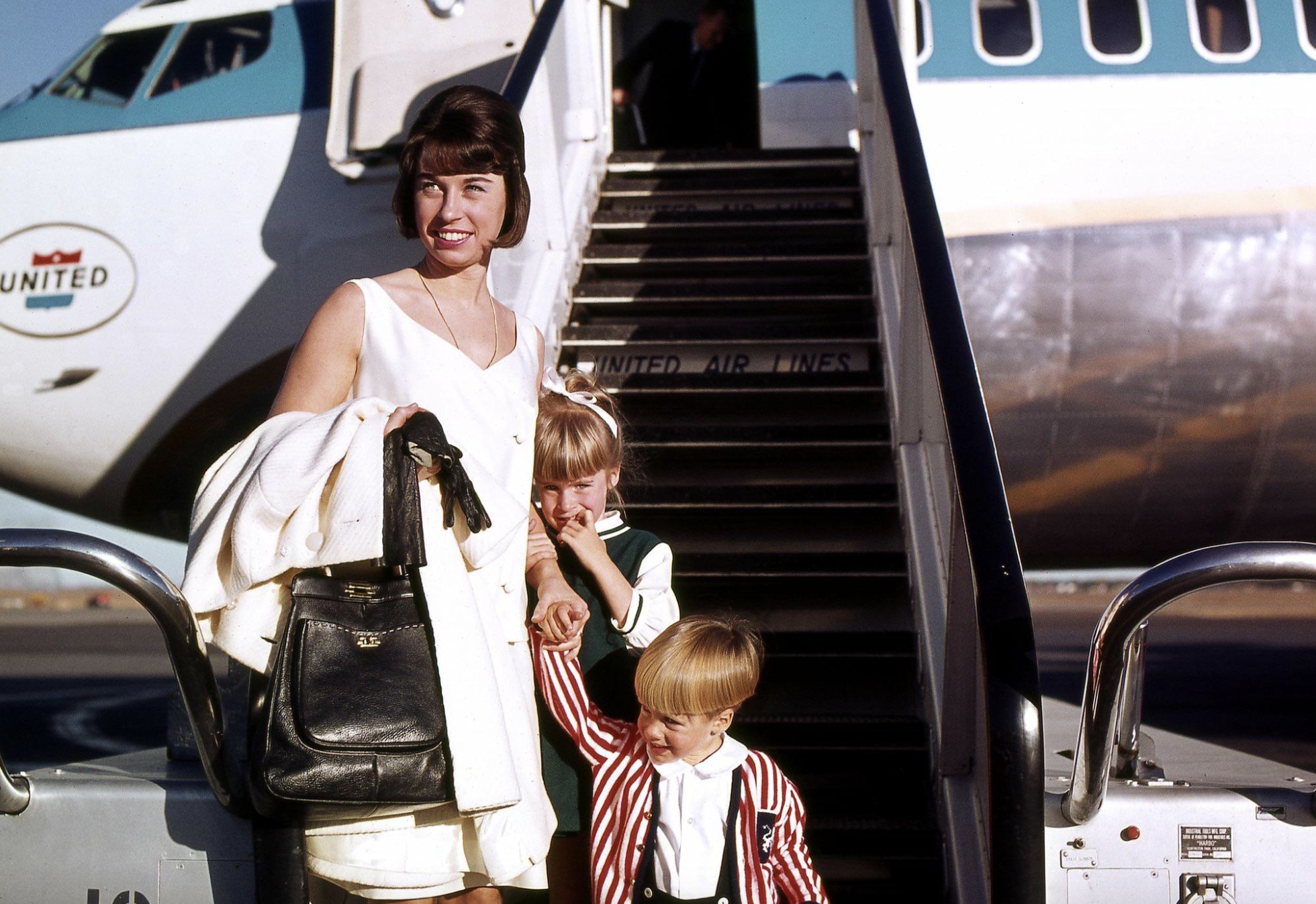 A woman and two young children stand at the base of a United Air Lines plane staircase.