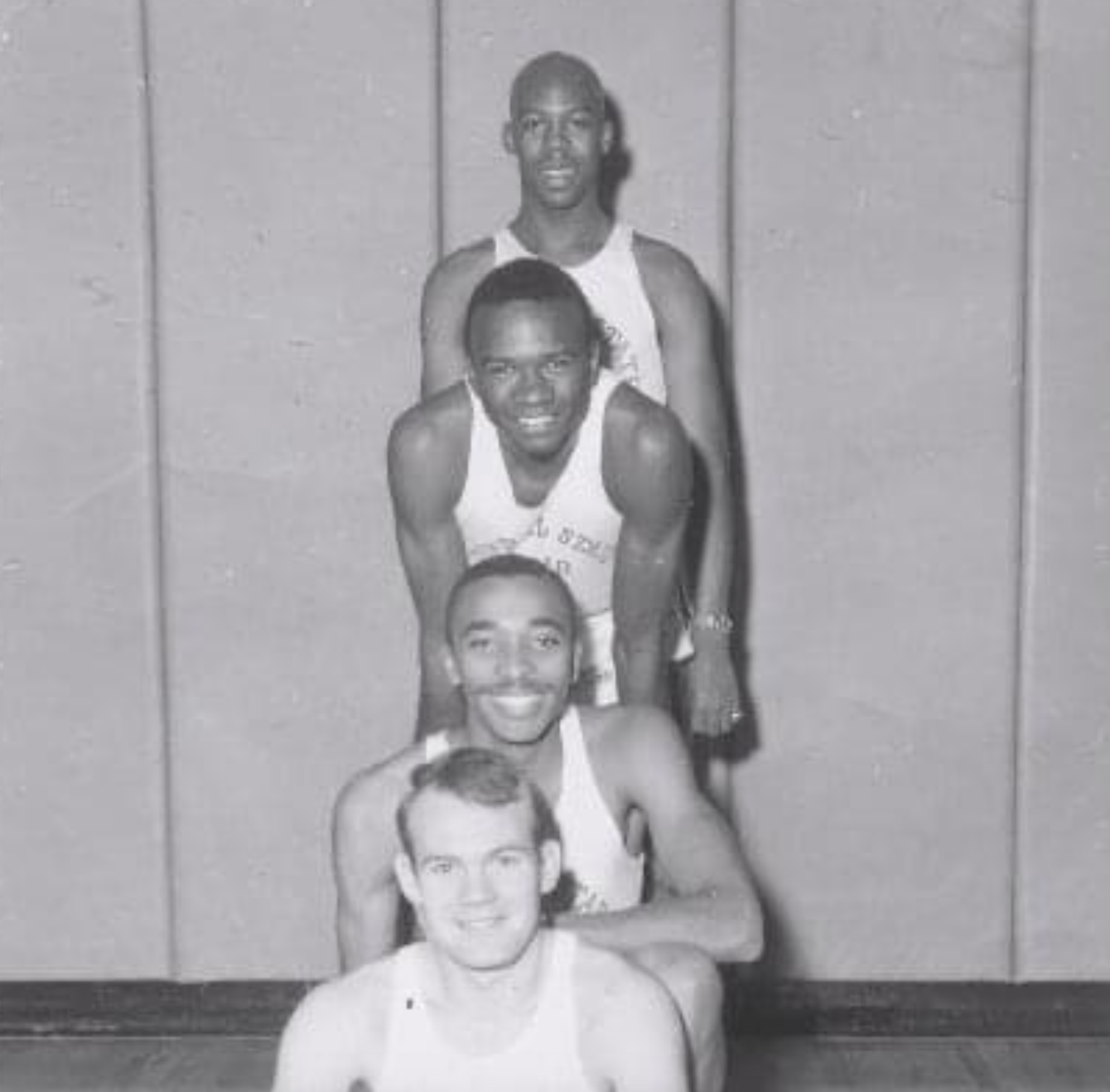 Four basketball players in jerseys posed in a vertical line, one behind the other.