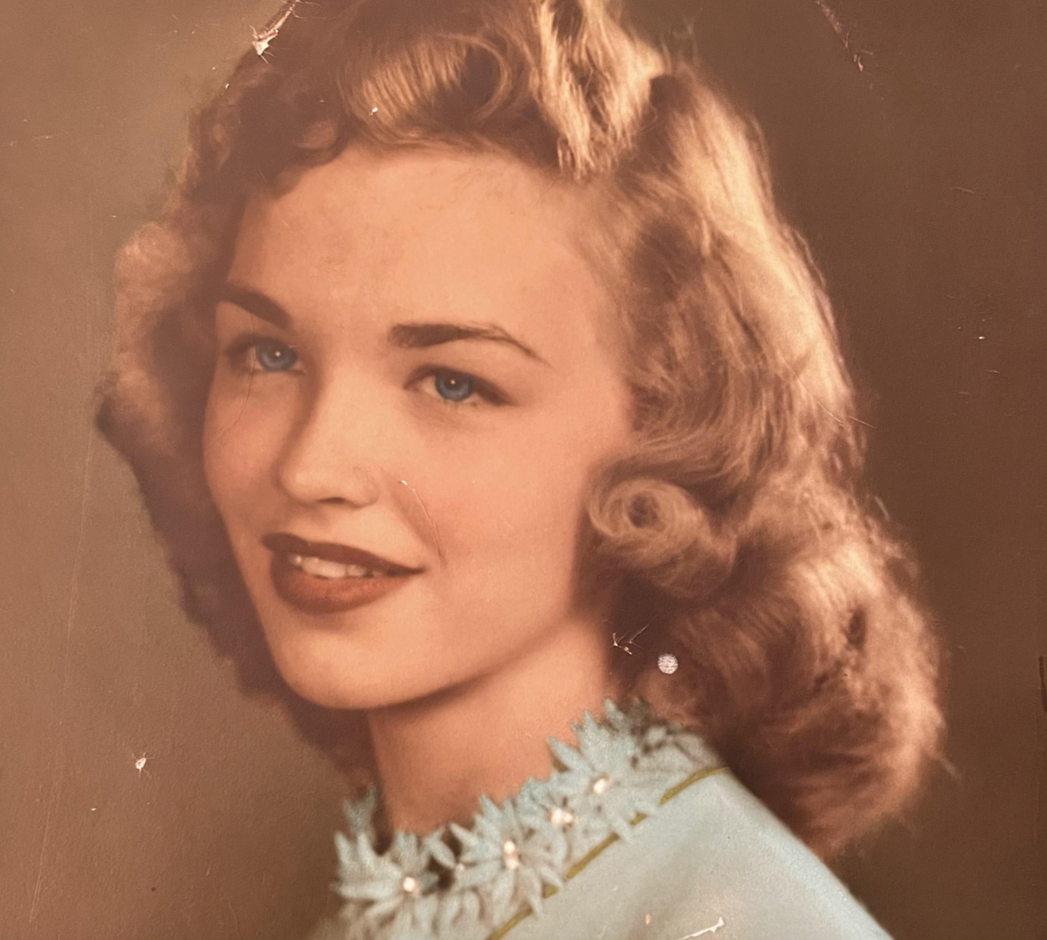 Portrait of a young woman with wavy hair wearing a light blue top with a floral-embellished collar.