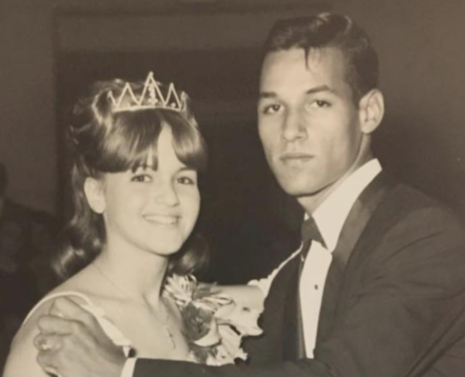 A sepia-toned vintage photograph of a young woman wearing a crown and a young man in a tuxedo, posing together for a formal dance.