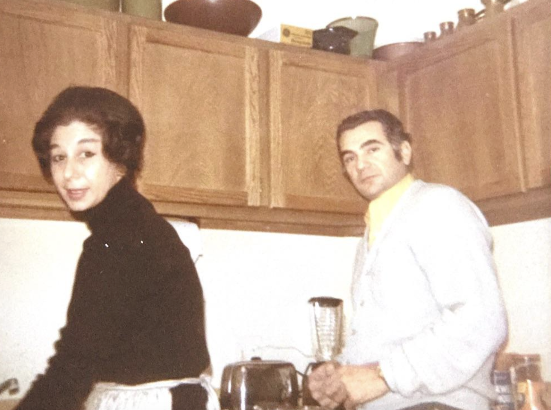 A woman and a man standing together in a kitchen in front of wooden cabinets.