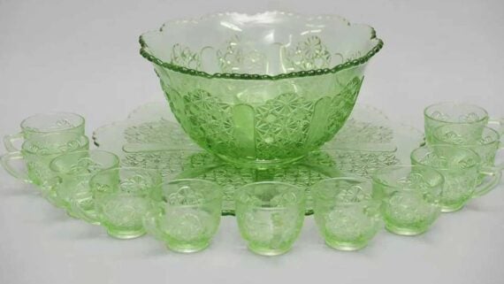 A green patterned glass punch bowl set with a large serving bowl on a matching platter, surrounded by eight small matching punch cups.