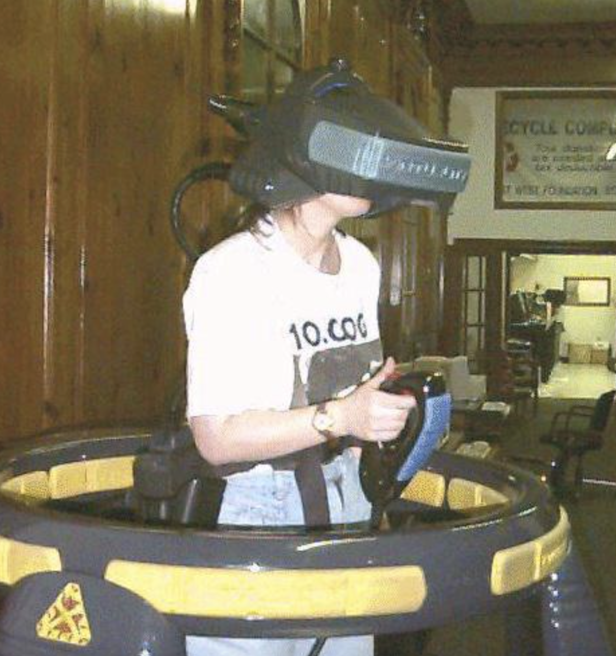 A person wearing a bulky virtual reality headset while standing inside a large circular platform and holding a handheld controller.