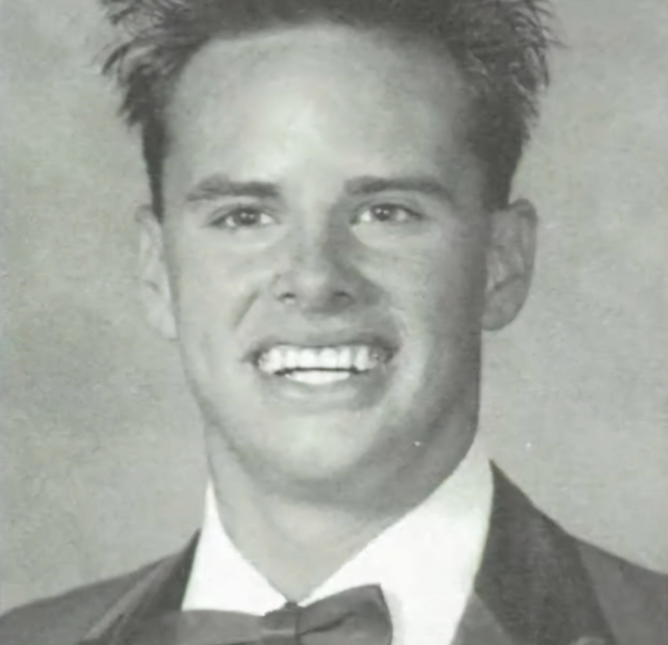 Black and white headshot of a young man smiling in a tuxedo and bow tie.